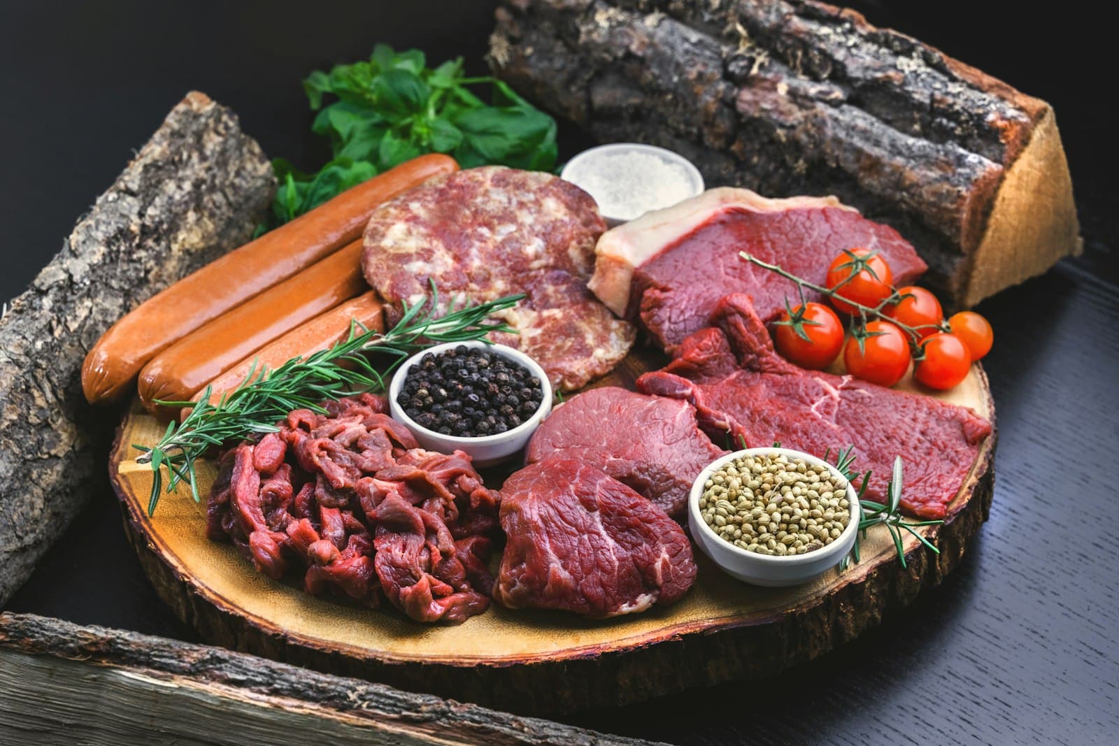 Tabla de madera con cortes de carne fresca, romero, tomates y especias sobre fondo oscuro